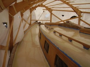 Here is the house and deck after two coats of two-part polyurethane paint.  You can see where I’ve cut holes in the tarp for both ventilation and cooling.  Other people are launching their boats.  